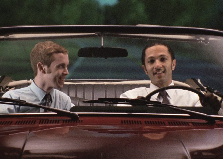 Two men riding in a convertible car.