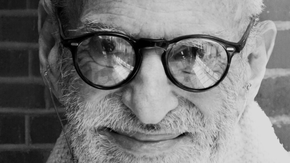Larry Kramer portrait, black and white close-up with glasses reflecting a building.