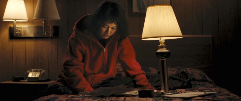 Kumiko, the treasure hunter, studies papers in a dimly lit motel room.