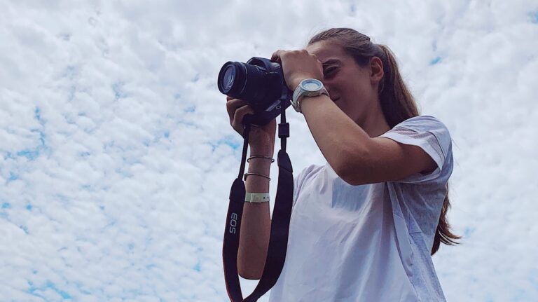 Girl taking photos with a Canon EOS camera against a cloudy sky.
