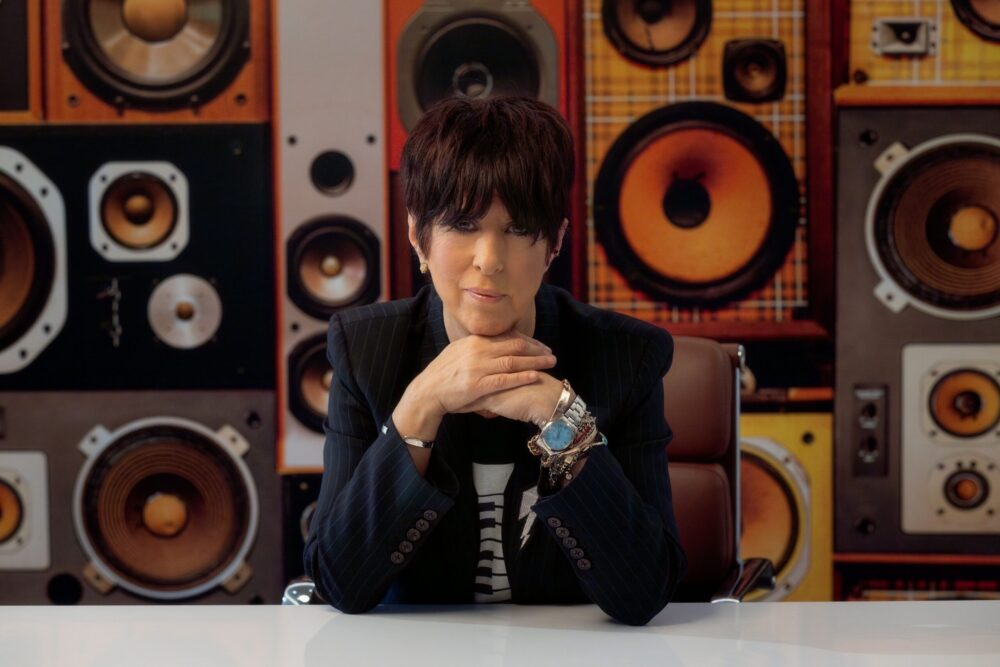 Diane Warren sits at a desk in front of a wall of speakers.