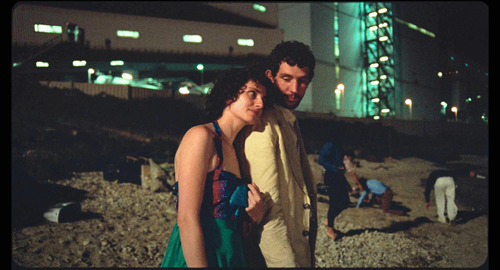 Couple embracing at night with industrial backdrop, possibly related to "La Chimera.