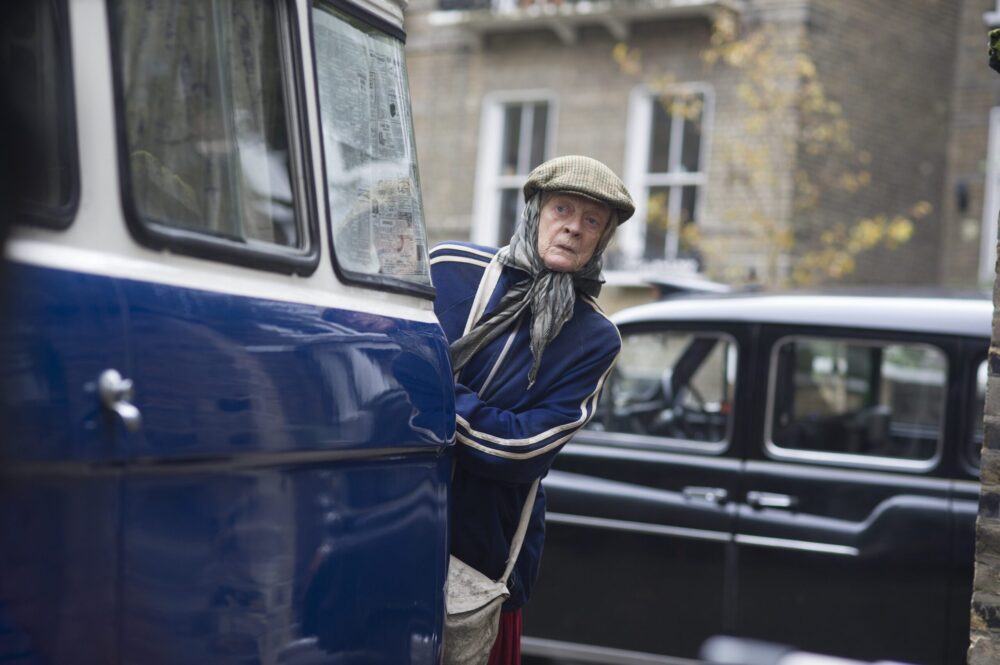 Maggie Smith as Miss Shepherd in The Lady in the Van, peering from behind a blue van.