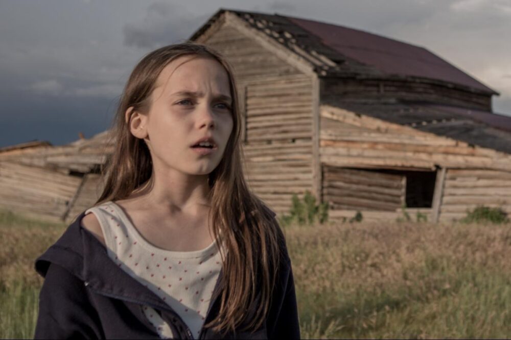 Young girl in front of an old barn, possibly related to the movie Lamb.