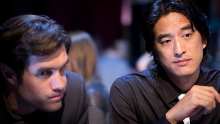 Two men in suits, one Asian, in a dimly lit setting.