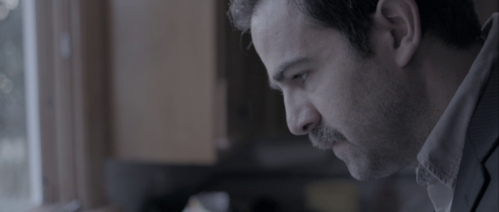 Man with a mustache looking down in thought.
