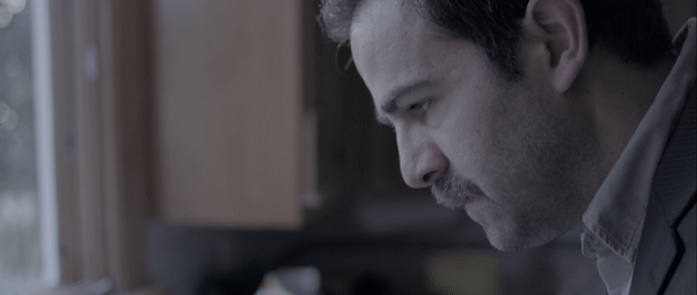 Man with a mustache looking down in thought.