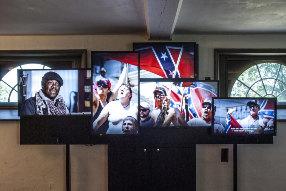 Art installation showing screens with Confederate flags and a Black man.