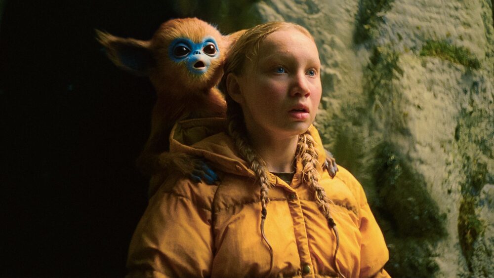 Girl in yellow jacket with monkey-like creature on her back, looking surprised. From "The Legend of Ochi.