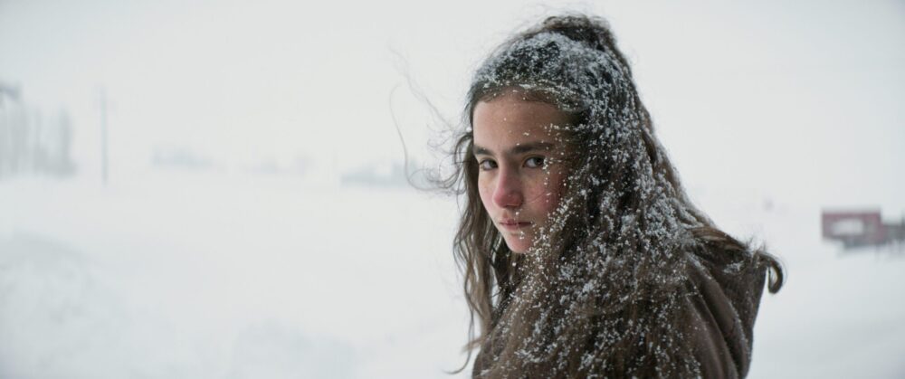 Girl with snow in hair looks back during winter.