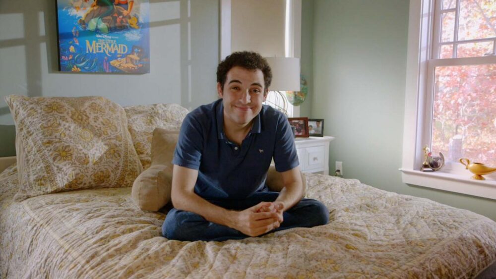 Owen Suskind, subject of "Life, Animated," sits cross-legged on a bed with a Little Mermaid poster.