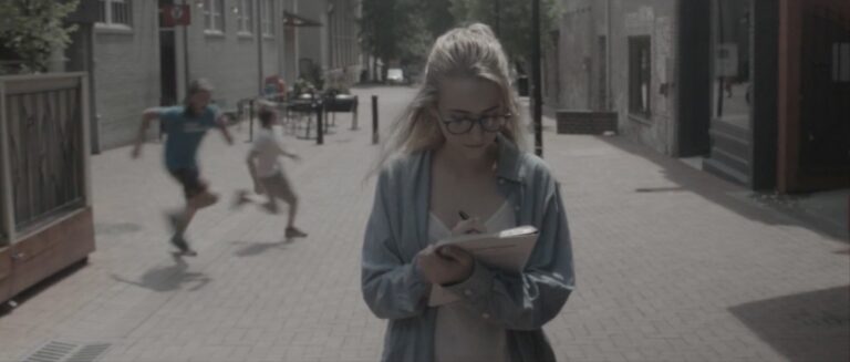 Woman with glasses writing in notebook, two boys running in background.