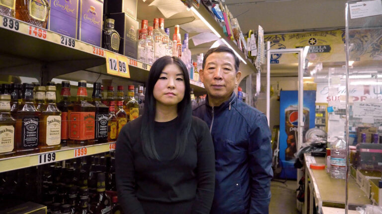 Owners of a local liquor store stand in front of shelves stocked with Crown Royal and Jack Daniel's.