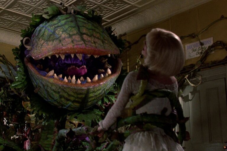 Audrey faces Audrey II in Little Shop of Horrors, the giant plant with a menacing open mouth and sharp teeth.