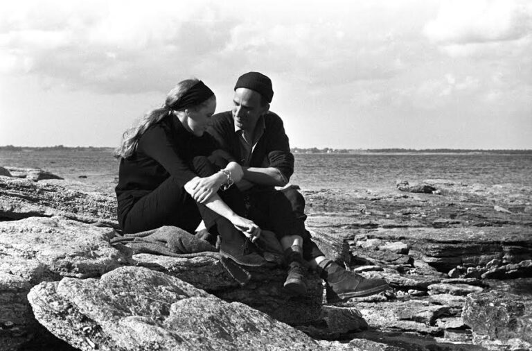 Liv Ullmann and Ingmar Bergman sitting on rocks by the sea.