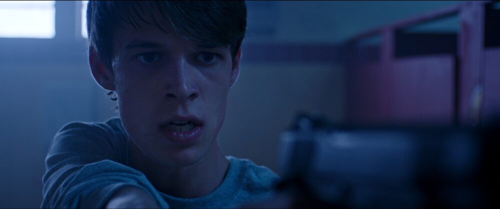 Young man holding a gun, tense expression.