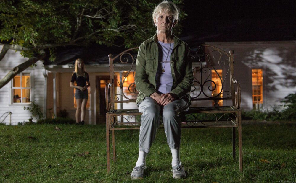 Elderly woman on bench at night, young girl stands near house. "The Looking Glass" mystery.