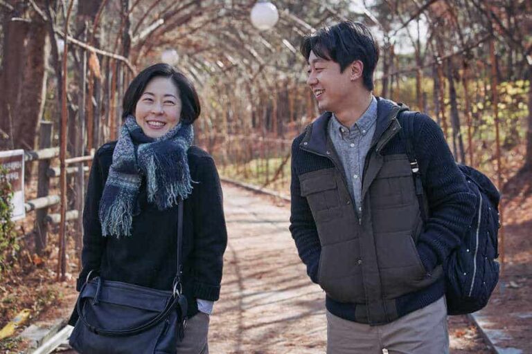 Smiling woman and man walking under an archway of trees.