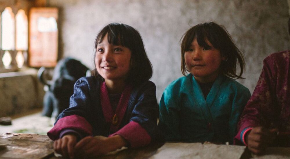 Two Bhutanese girls in traditional clothing smile in a classroom in Lunana.