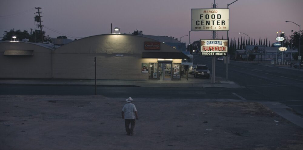 Man walks towards Merced Food Center and Carniceria Superior at dusk. MoneyGram sign visible.