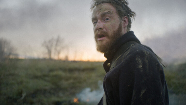Civil War soldier with dirt on his face looks back during battle.