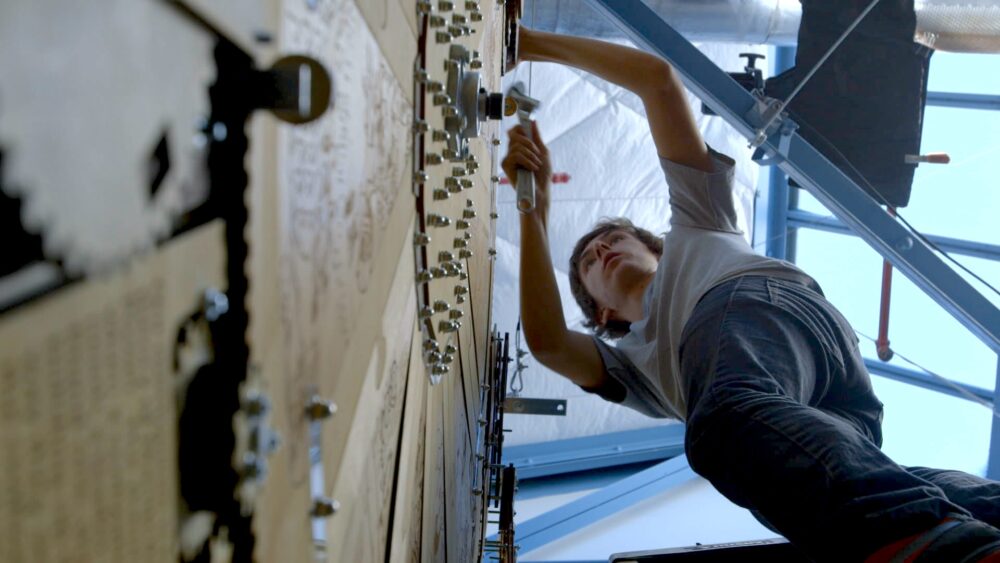 Man working on a large mechanical art installation with gears and intricate designs.