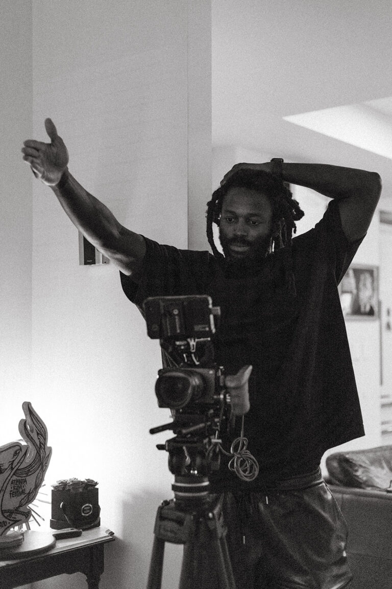 Filmmaker Maba Ba gesturing behind a professional camera setup in a home studio.