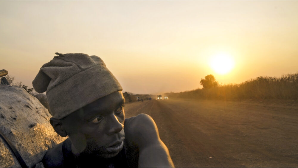 Man carrying Makala (charcoal) on a dusty road at sunset.