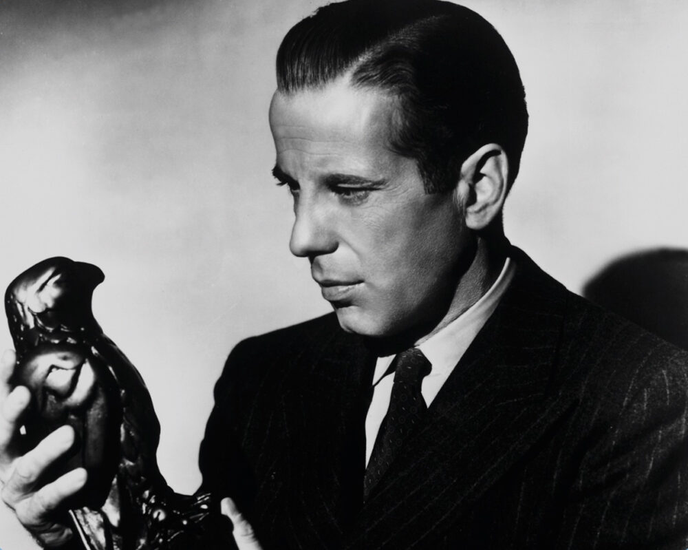 Humphrey Bogart in "The Maltese Falcon" holding the falcon statue, looking intently at it.