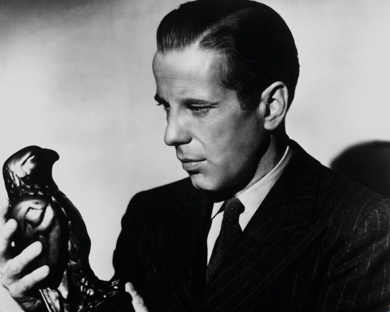 Humphrey Bogart in "The Maltese Falcon" holding the falcon statue, looking intently at it.