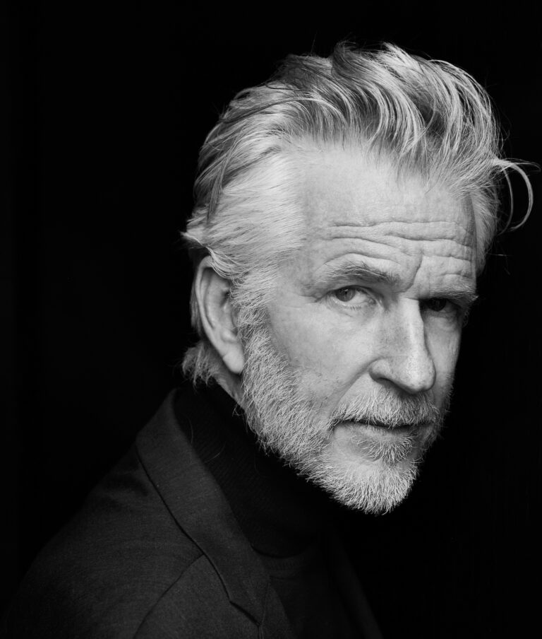 Matthew Modine portrait. Black and white studio shot of the actor with gray hair and beard.