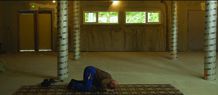 Man praying on a rug in a sparse, unfinished room.