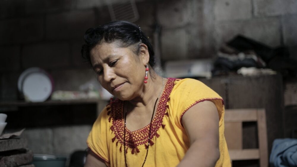 Woman in yellow top, possibly a mom, in a rustic kitchen setting.