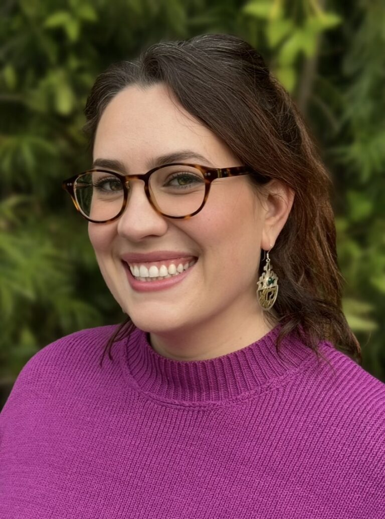 Smiling woman, Montana Mann, wearing glasses and a purple sweater.