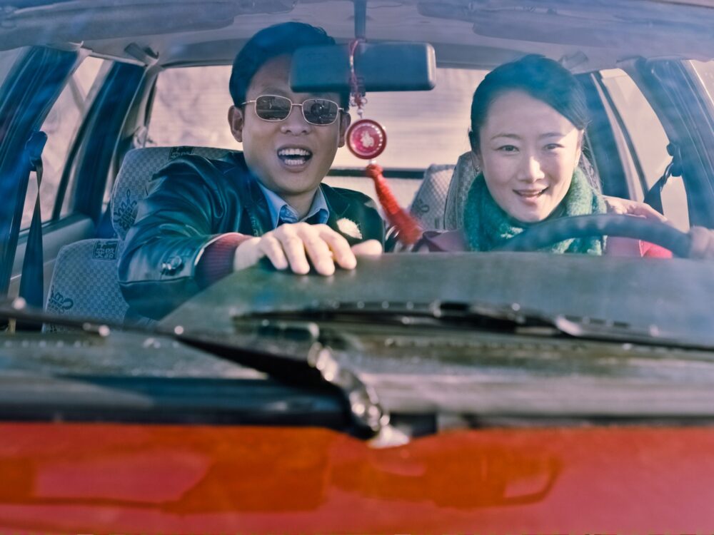 Couple in car from Jia Zhangke's "Mountains May Depart," smiling at the camera.