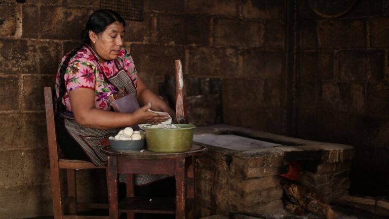 Woman making tortillas in a rustic kitchen.