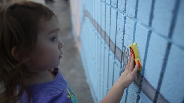 Little girl touching a butterfly painted on a blue brick wall mural.