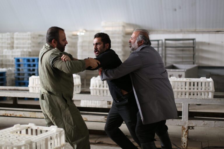 Scene from "No Date, No Signature" showing two men restraining a third in an industrial setting.