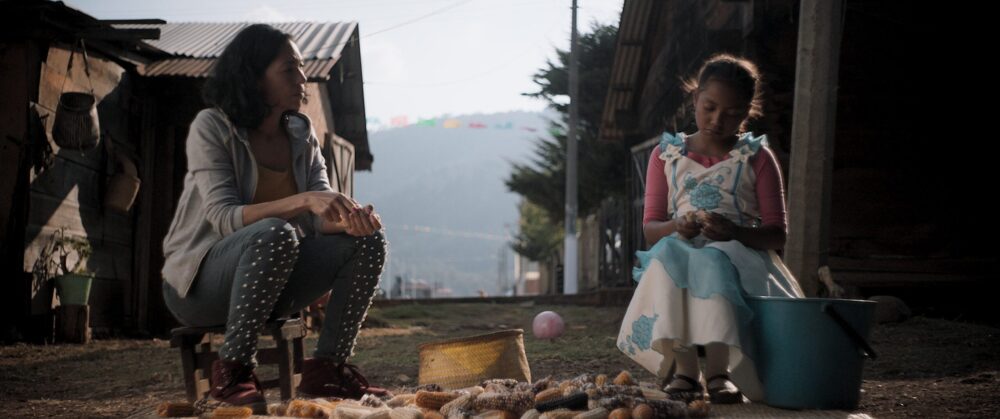 Woman and child preparing corn in a rural setting.