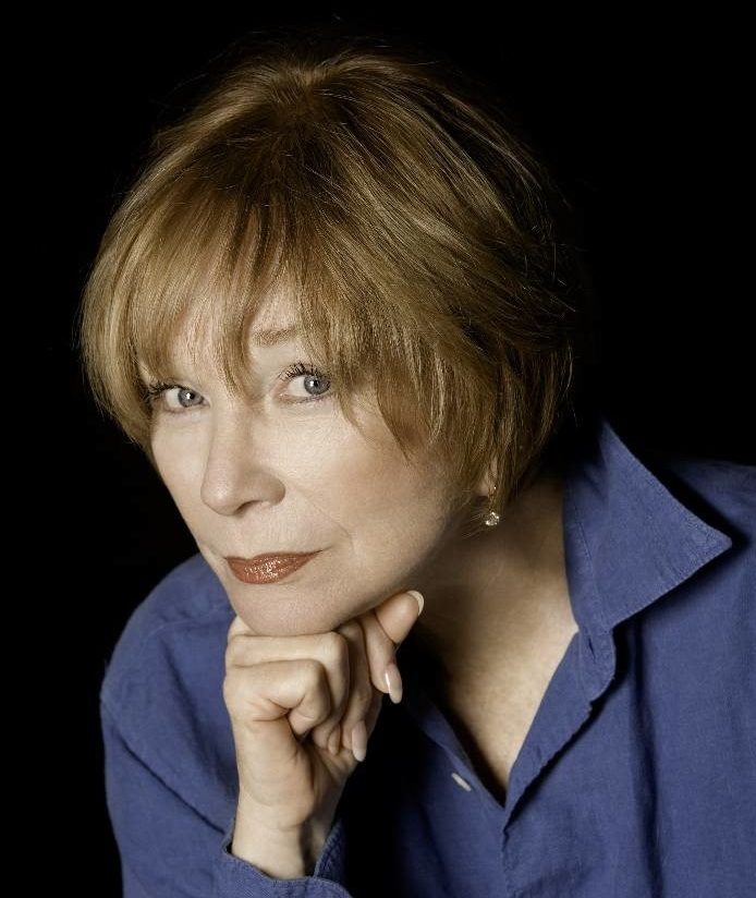 Portrait of actress Shirley MacLaine with auburn hair, wearing a blue shirt.