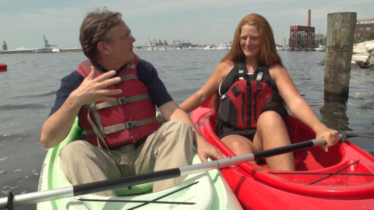 Kayakers paddling in ocean city harbor with urban skyline in background.