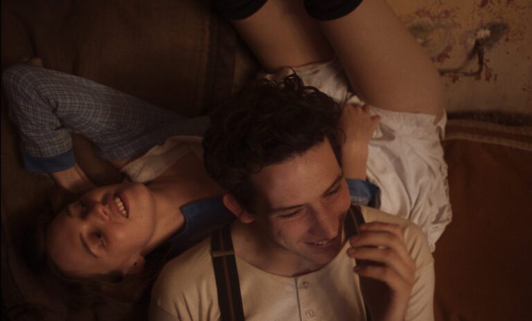 Couple smiling, lounging on a couch in "Mothering Sunday