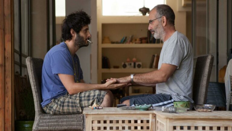 Still from "One Week and a Day" showing a father and son holding hands in a moment of connection.