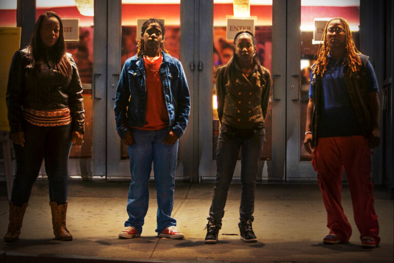 Four people stand in front of a building at night. "Enter" sign is visible.