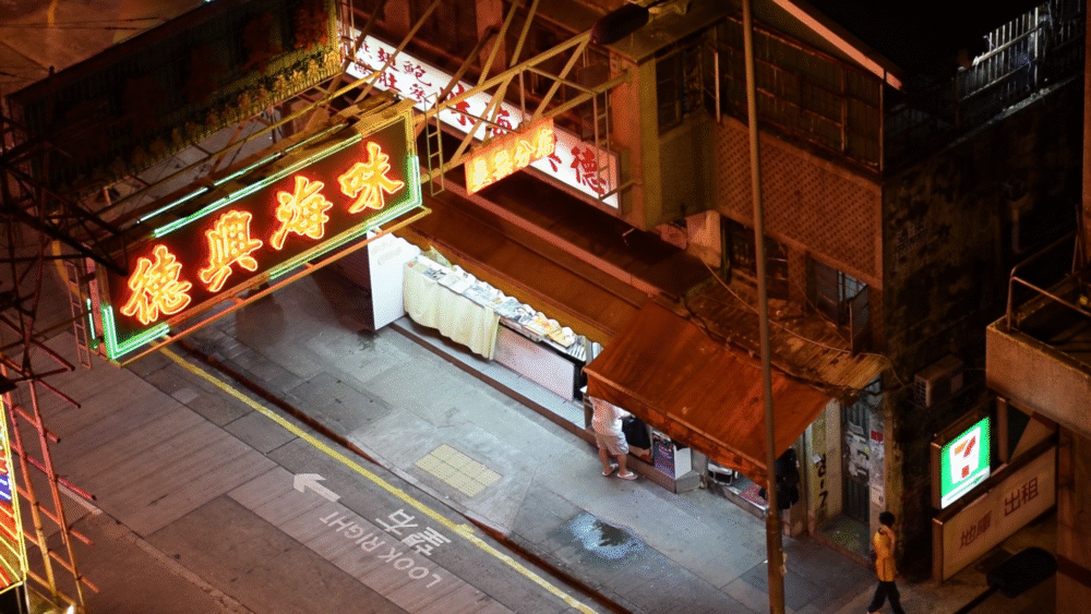 Hong Kong street scene at night featuring neon signs and a small shop.
