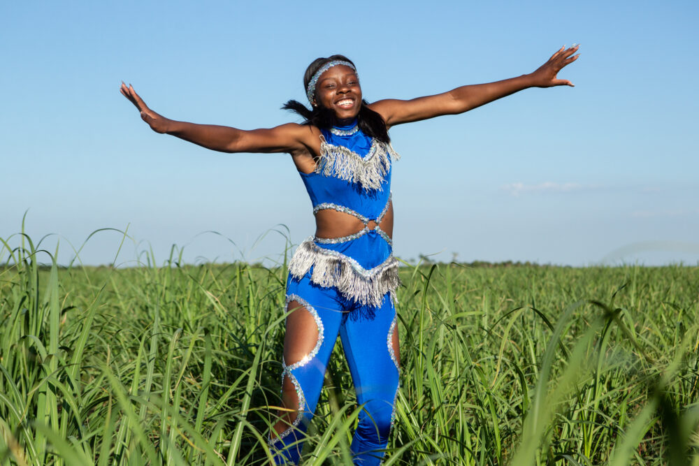 Pahokee: Smiling woman in blue costume with silver fringe, arms outstretched in a grassy field.