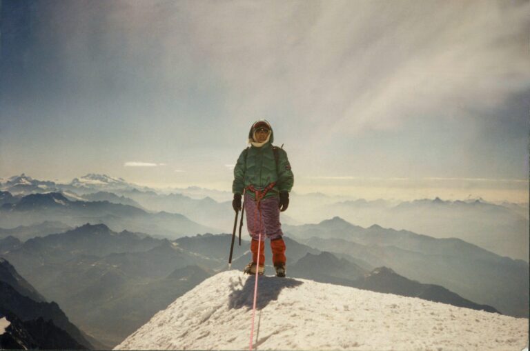 Mountaineer on a snowy peak with mountain range backdrop. Everest shadow.