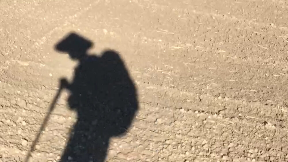 Shadow of a pilgrim with hat, backpack, and walking stick on a dusty path.