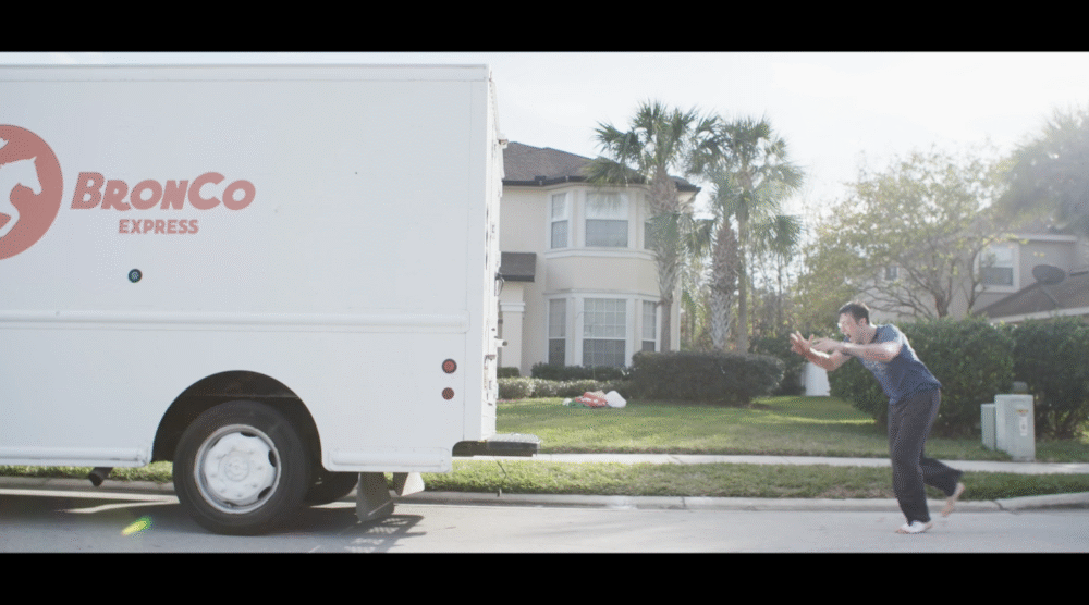 Man chasing a Bronco Express delivery truck on a residential street.