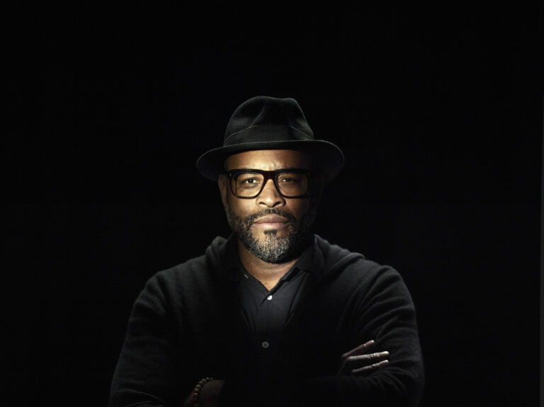 Kwaku Alston portrait in a black hat and glasses, arms crossed.